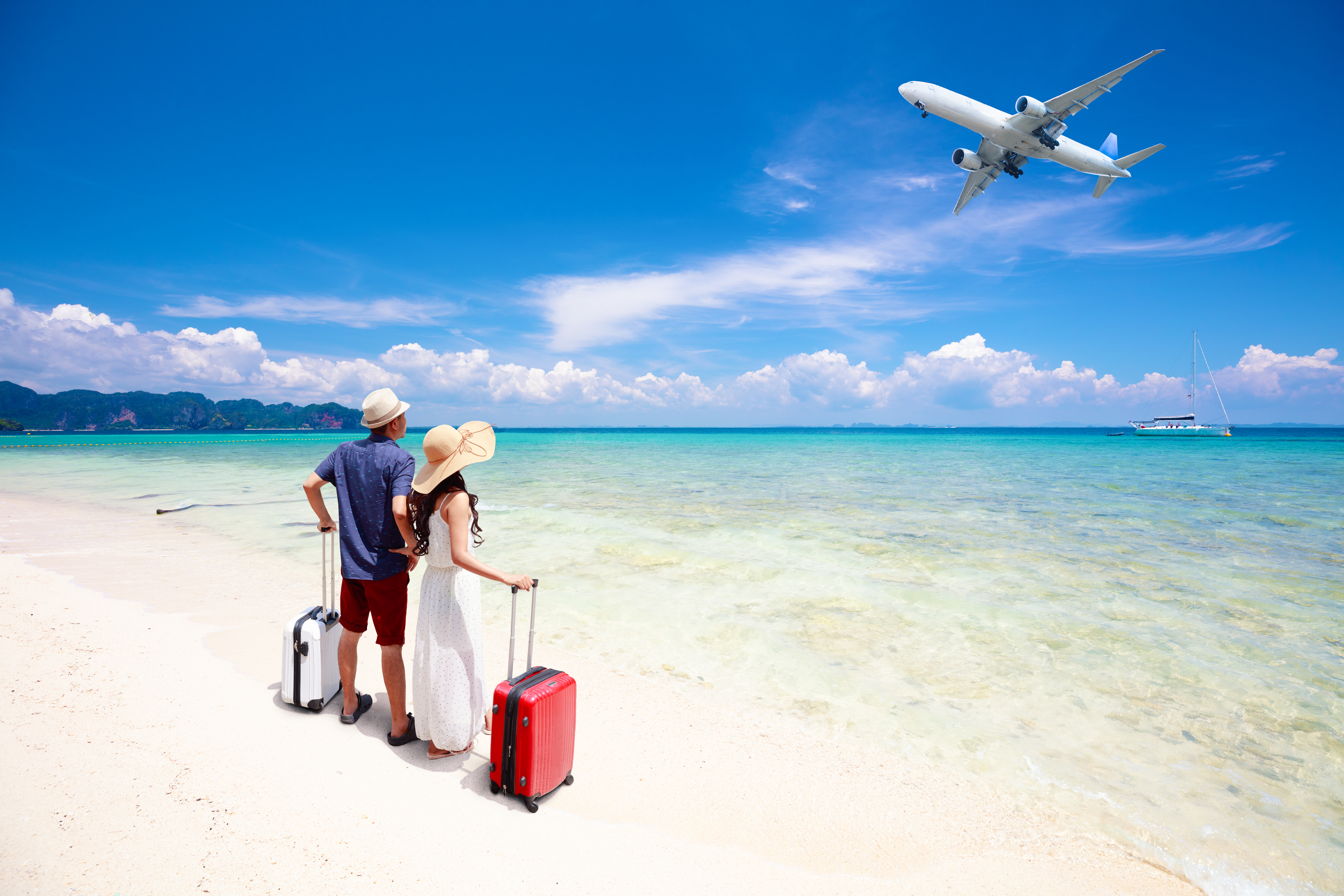 couple with luggage on beach looking at an airplane