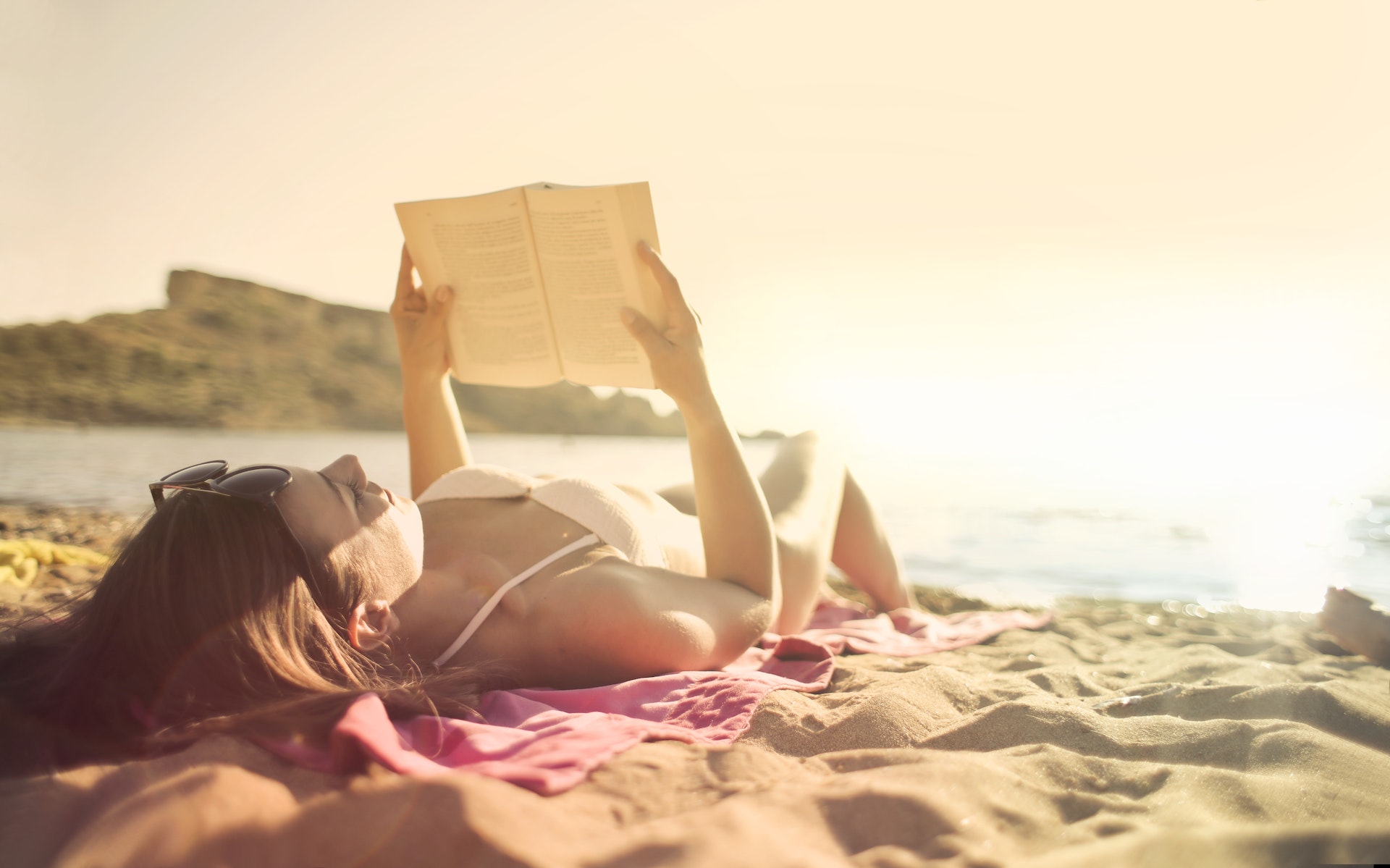 Woman lying on beach reading book