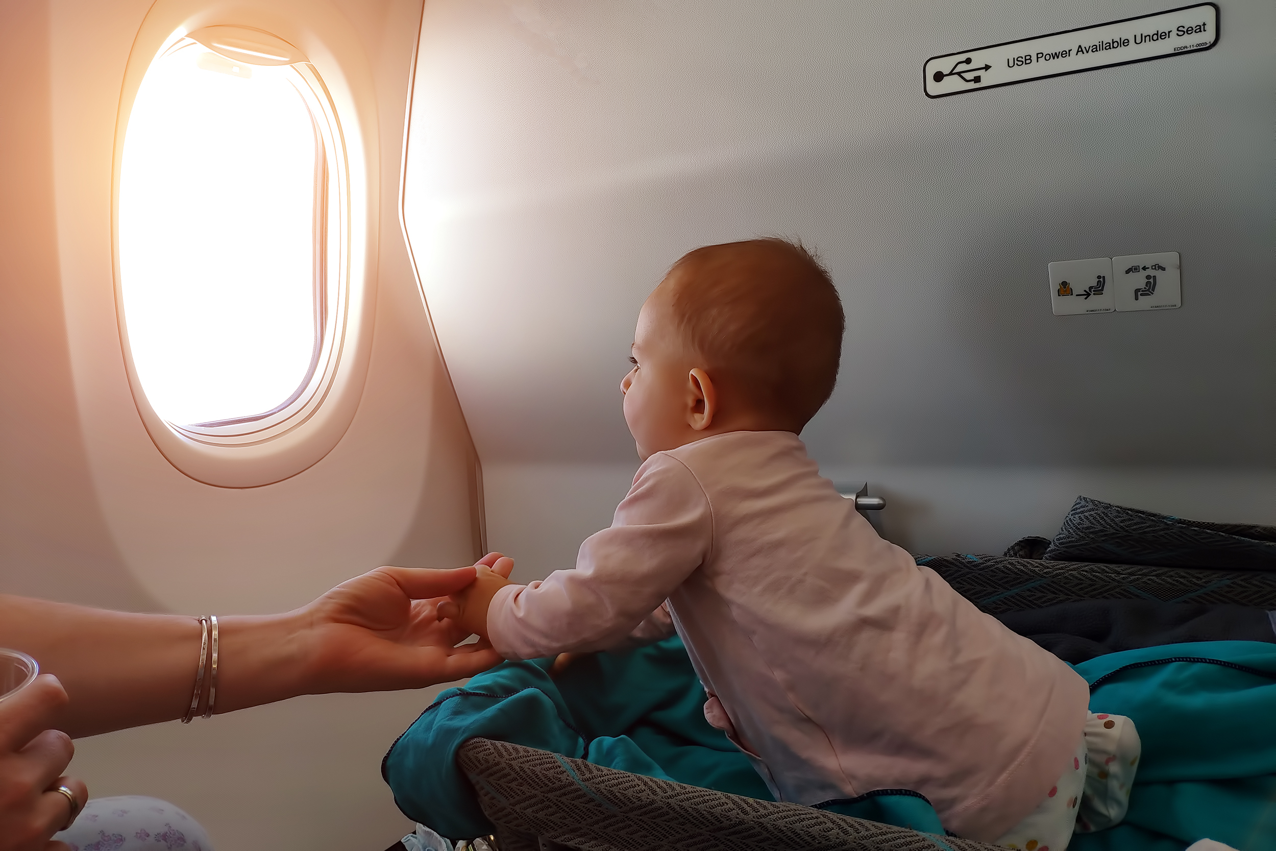 Baby looking out airplane window in bassinet