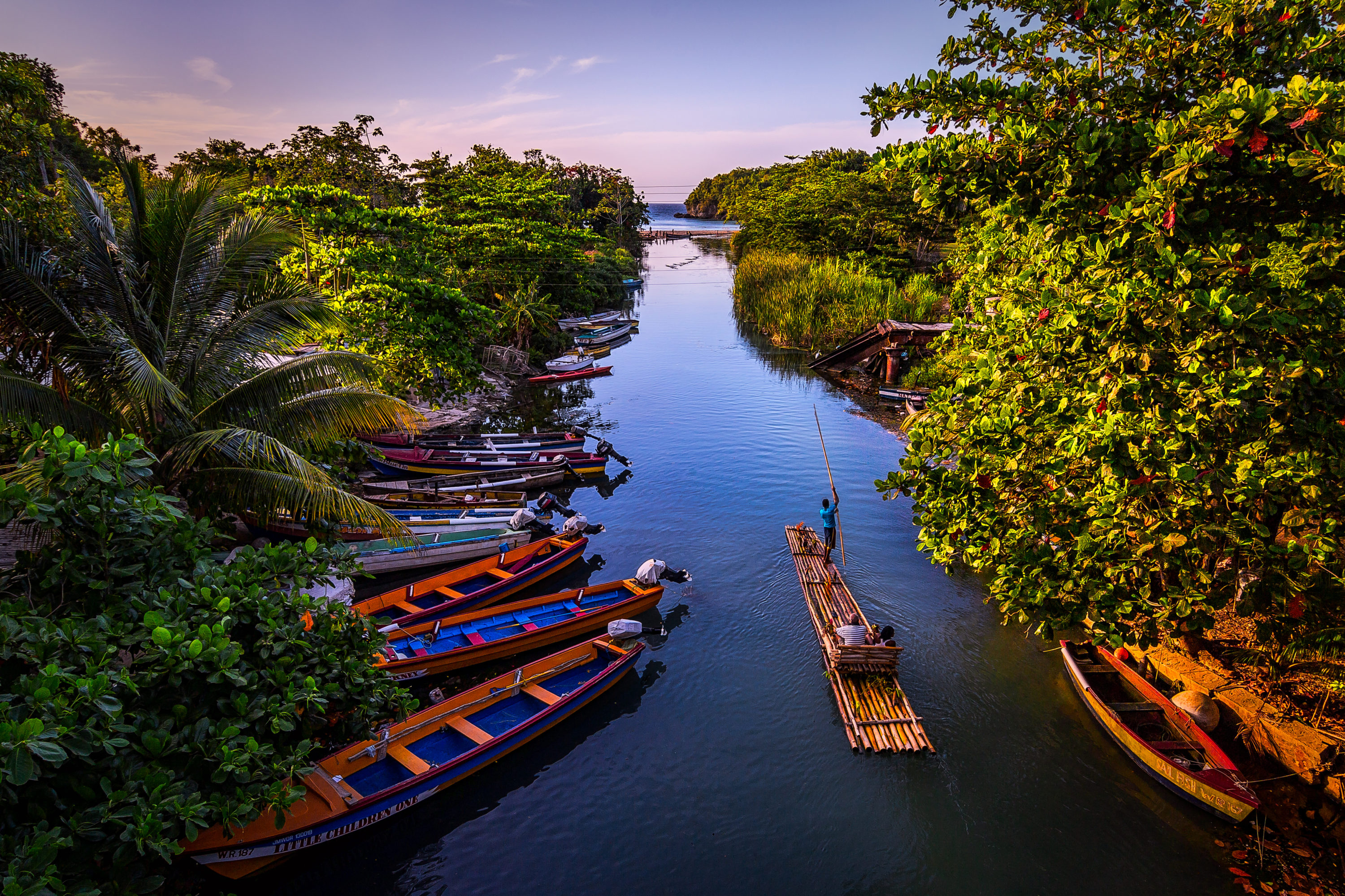 Rafts line the banks of a narrow, tree-lined river.