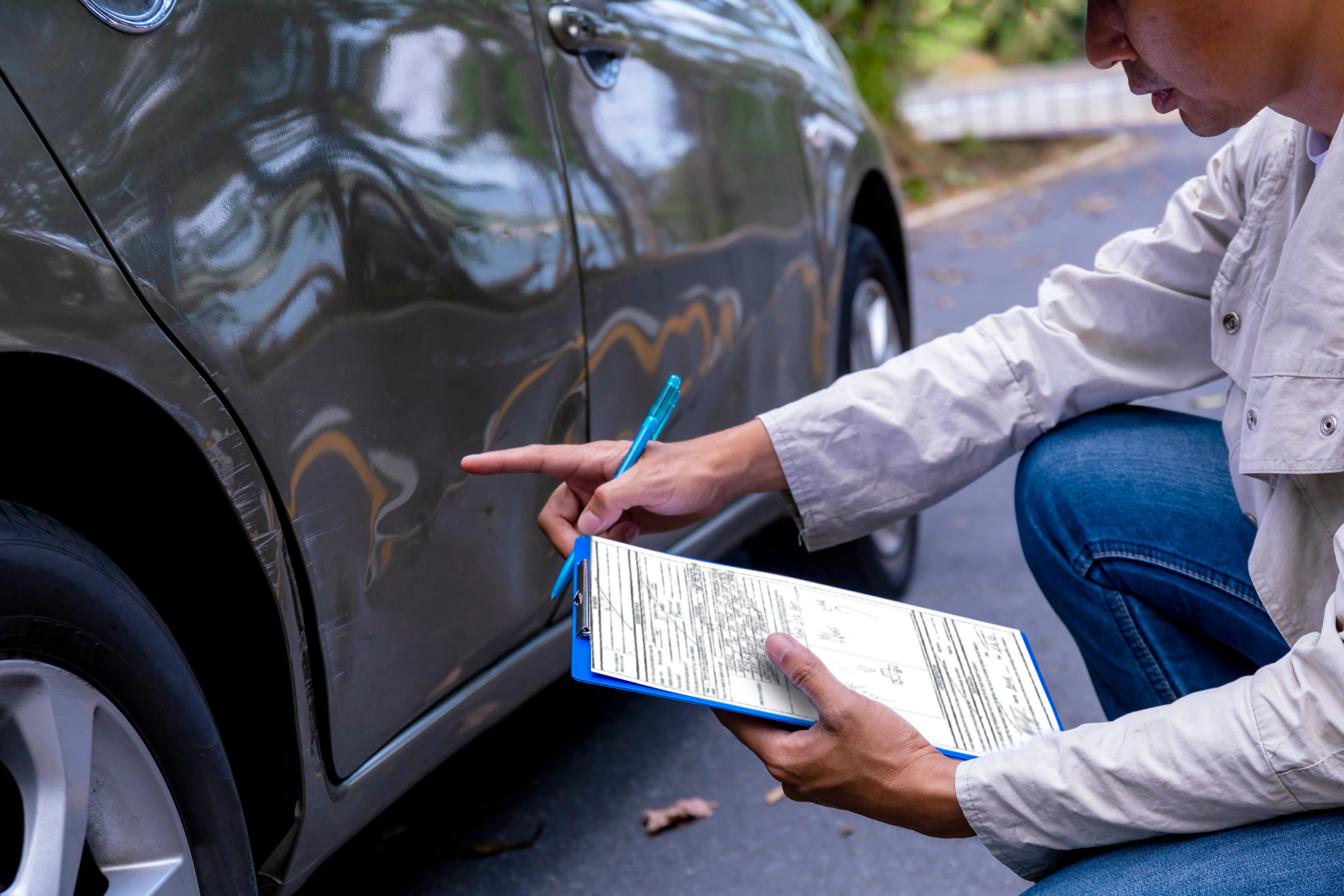 Insurance agent writing on clipboard while examining car after accident claim being assessed and processed