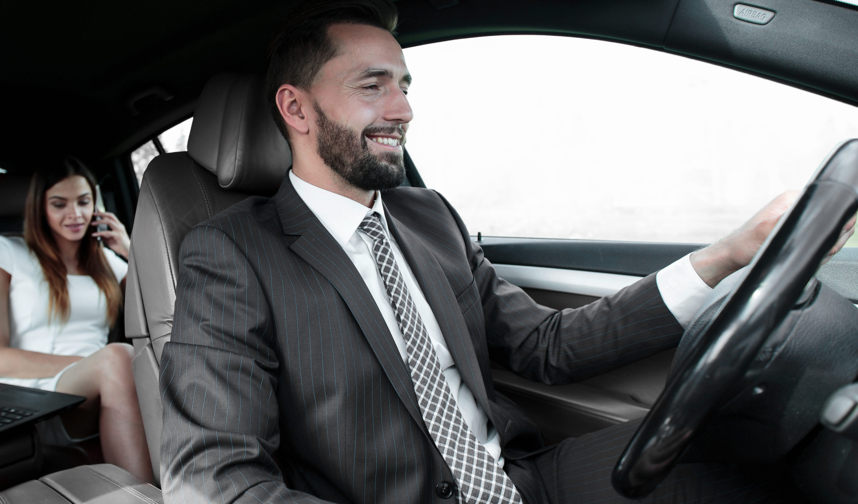 Man driving car in suit with female passenger on phone