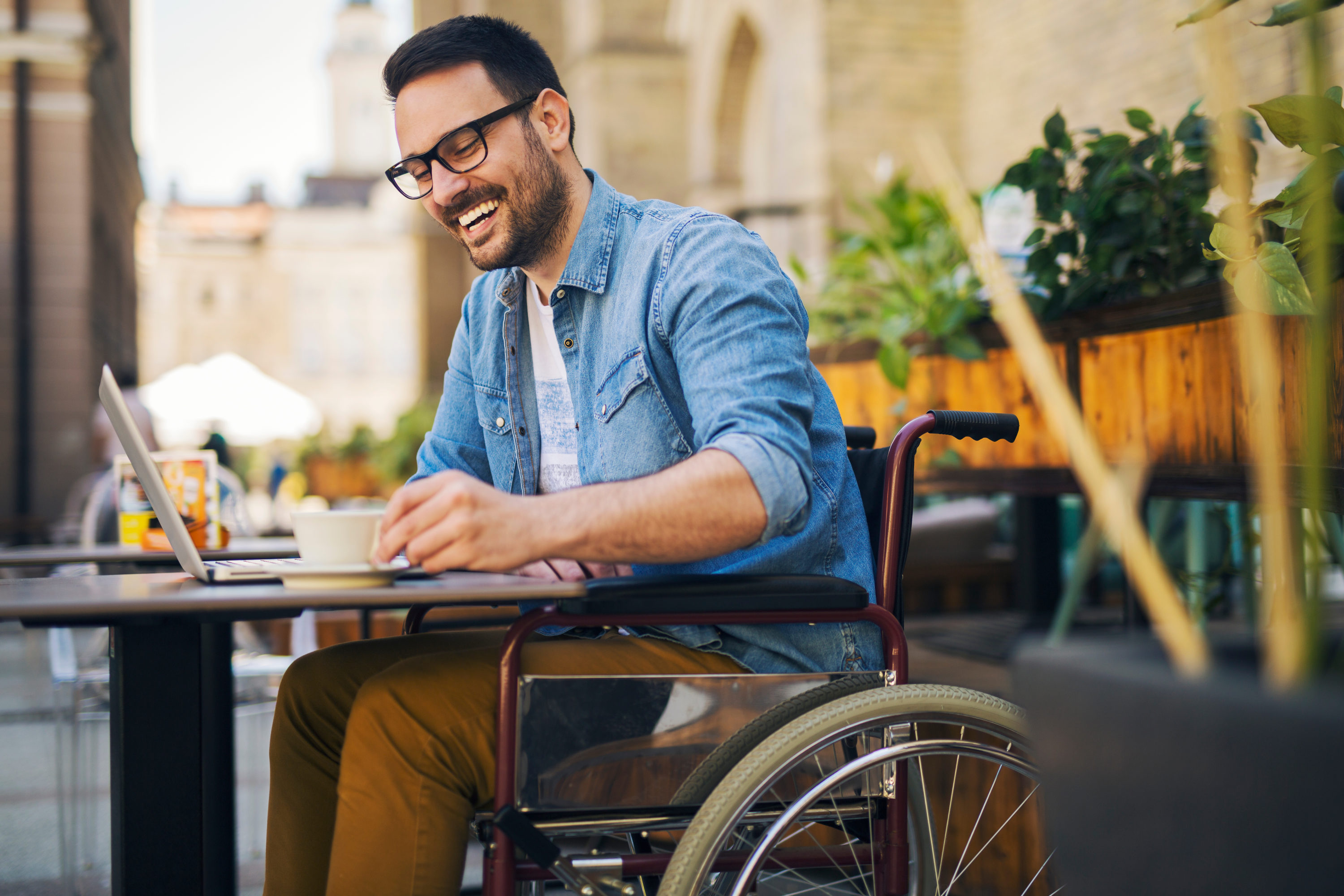 Man in wheelchair laughing at cafe with laptop Man in wheelchair laughing at cafe with laptop
