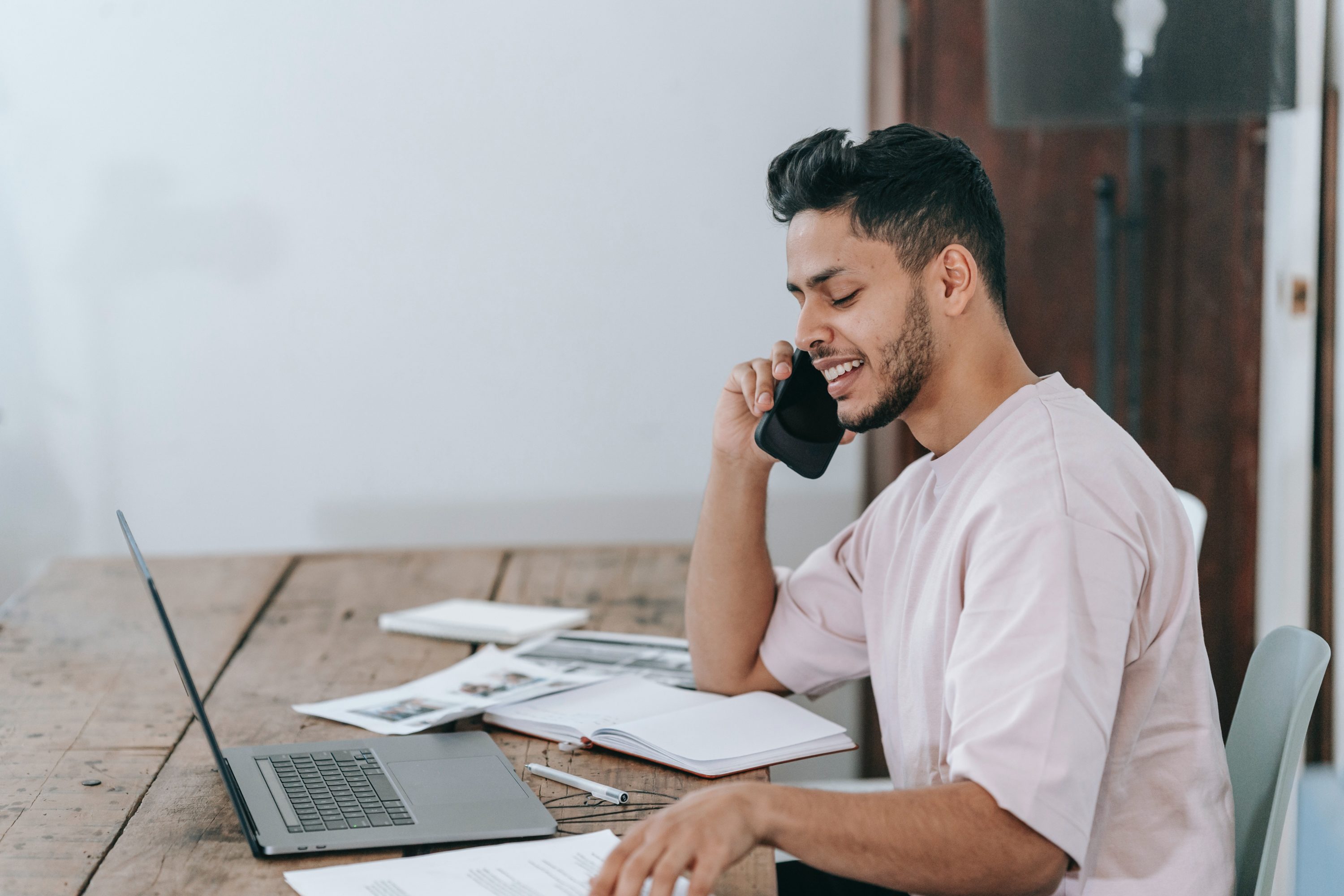 Man at his desk with a laptop and papers making a phone call