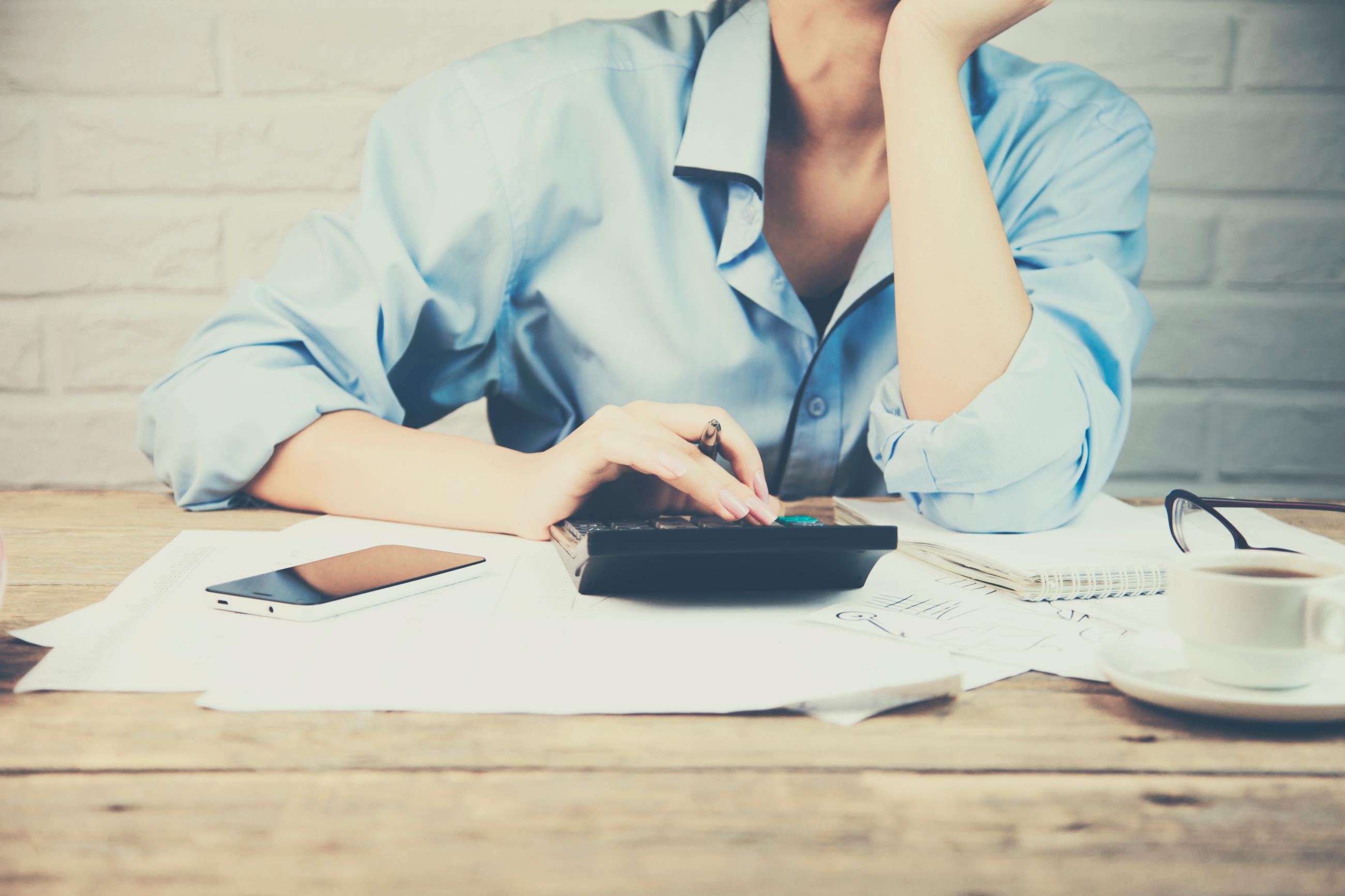 Woman working on taxes with a calculator phone coffee and glasses
