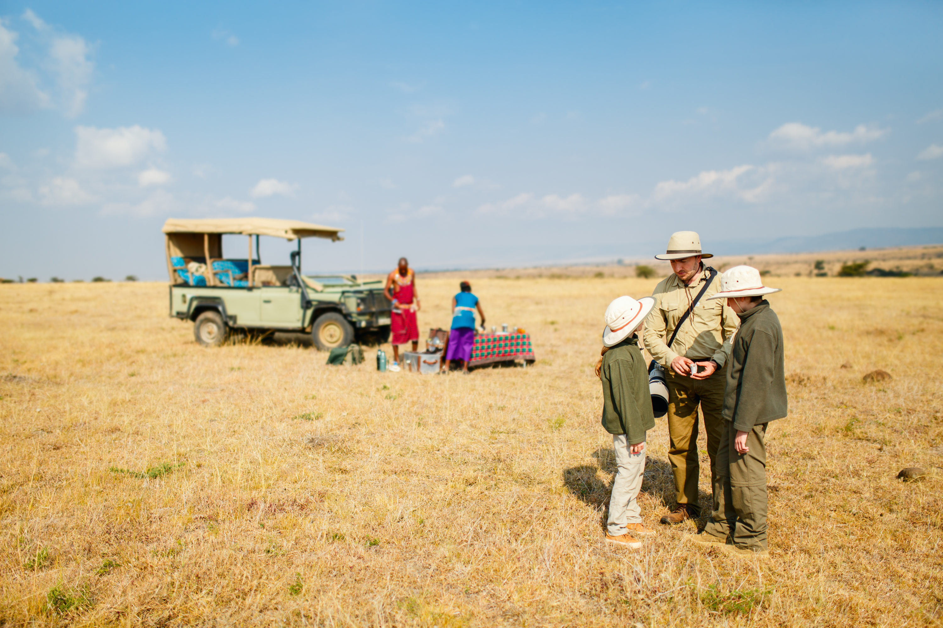 Family of father and kids on African safari vacation enjoying bush breakfast.