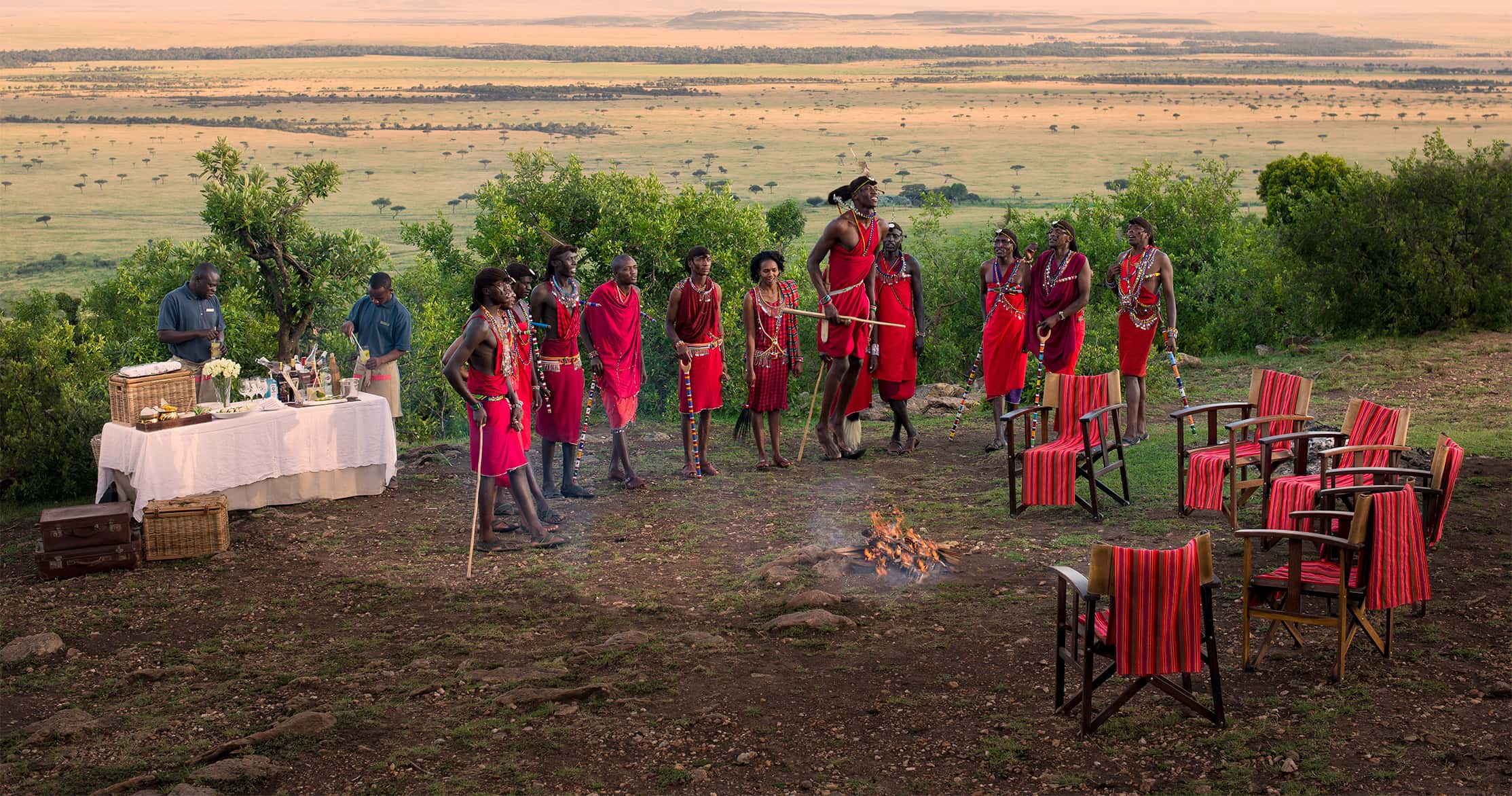 The Maasai people in the Maasai Mara Natural Reserve dressed in red and standing around a small fire.