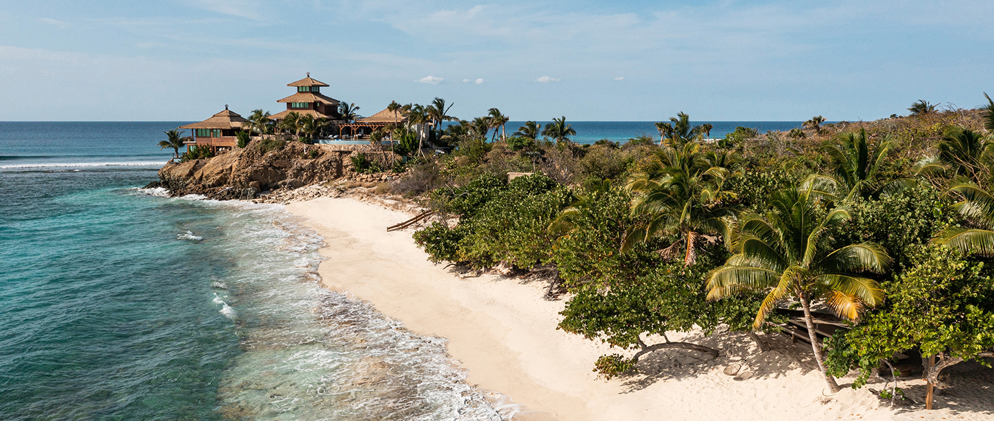 A photo of Necker Island with beach and lush landscape in the foreground. A photo of Necker Island with beach and lush landscape in the foreground.
