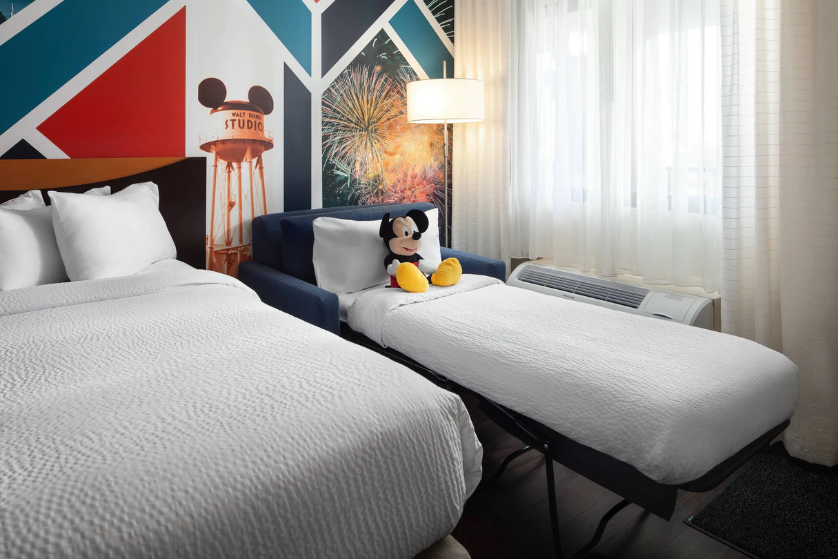 Guestroom at Fairfiled Anaheim A photo of a guestroom at Fairfiled Anaheim Resort shows a pullout sofa bed with a Mickey Mouse stuffed animal against a pillow.