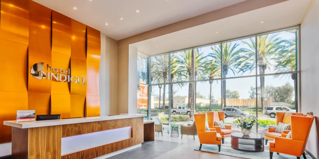 Hotel Indigo Anaheim lobby The lobby at Hotel Indigo Anaheim has a bright, orange textured wall behind the hotel lobby with seating to the left in front floor to ceiling windows.