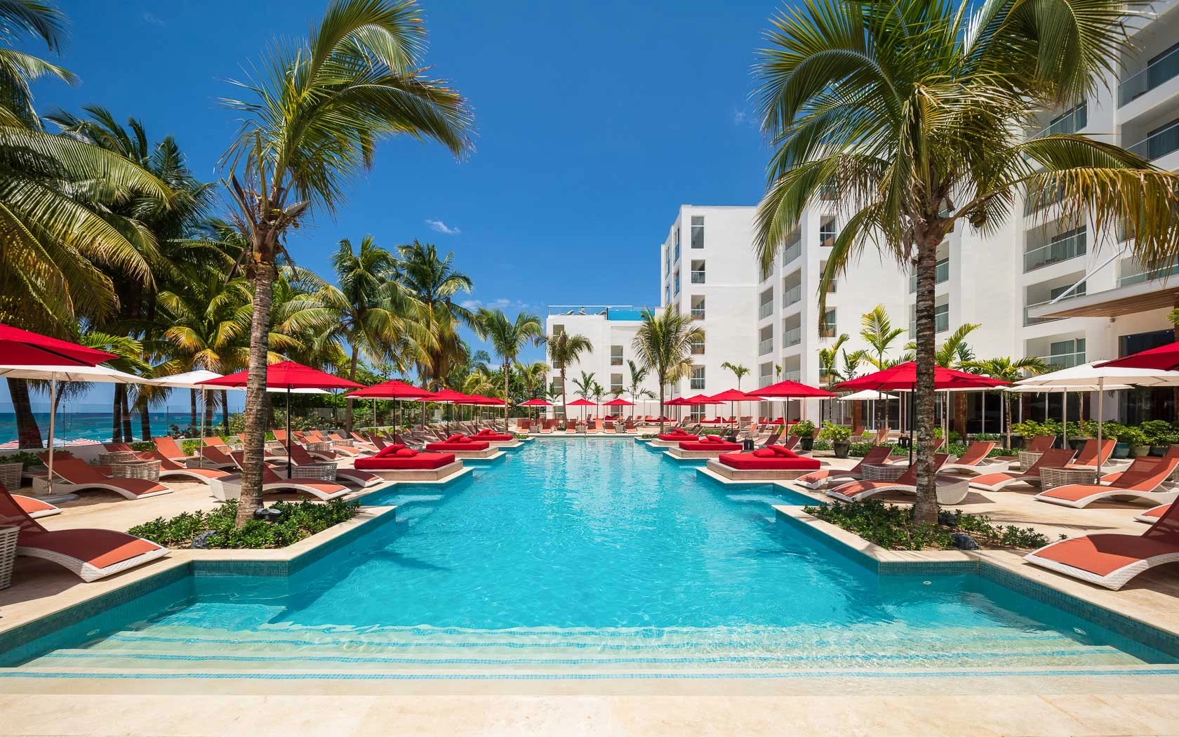S Hotel Jamaica The pool area at S Hotel Jamaica surrounded by red umbrellas and lounge chairs with palm trees.