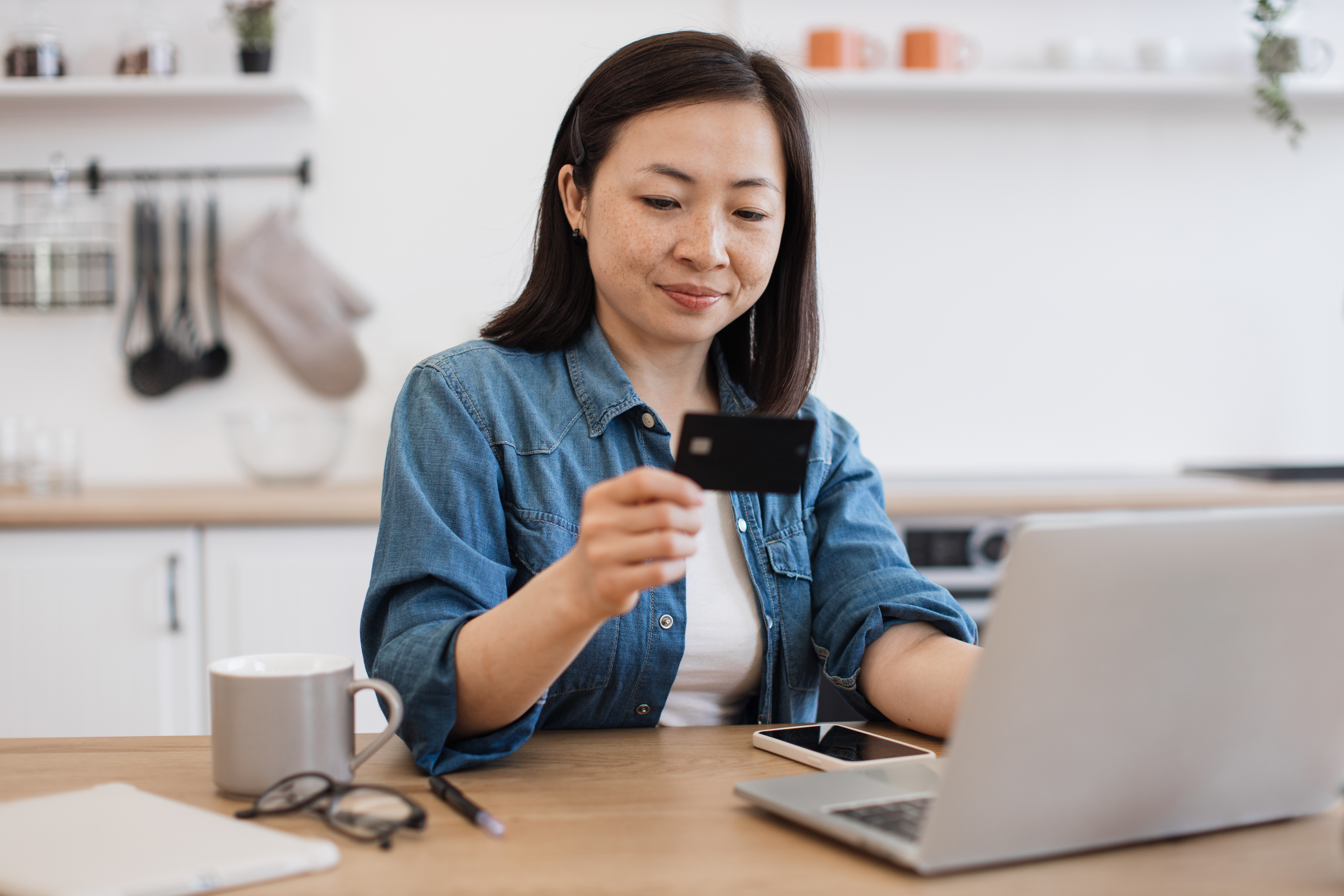 Female with credit card teleworking via laptop in kitchen